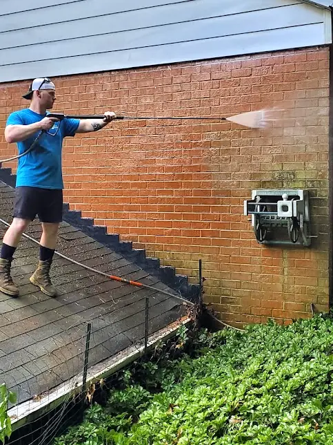 Ultimate Powerwash technician on a roof, pressure washing a red brick wall