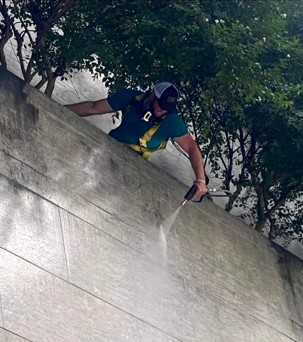 Close-up of a harnessed crew member pressure washing a stone facade from above