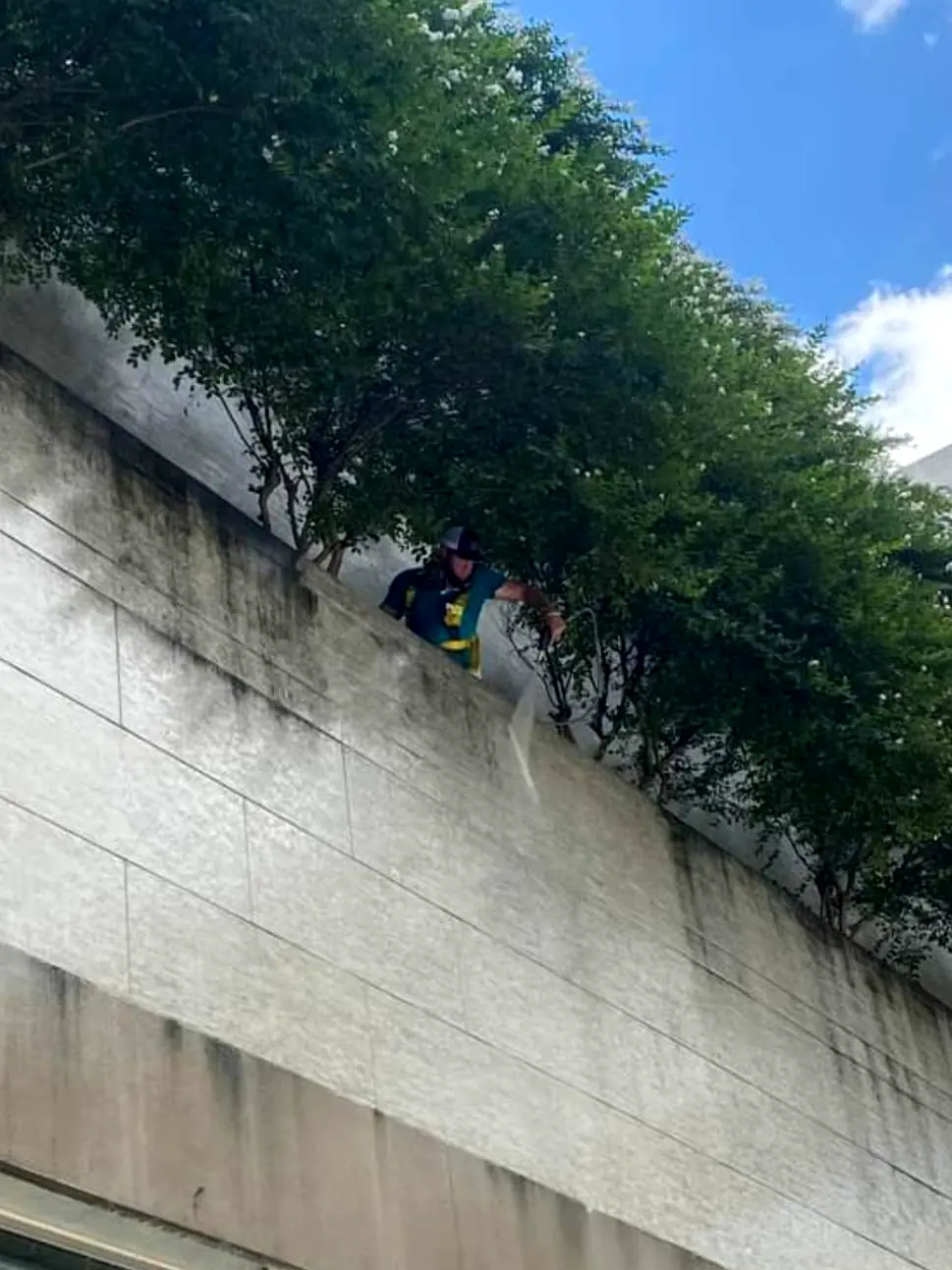 Crew member working from a rooftop planter ledge to wash dark streaks off a commercial stone wall