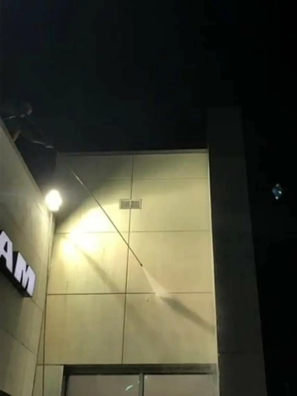 Night wash of a commercial building facade under floodlights, using an extension wand from the roof