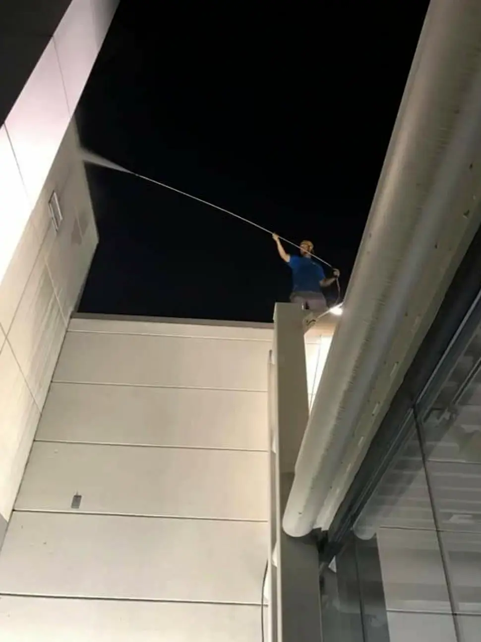 Crew member on a commercial roof at night, reaching an upper facade with a long extension wand