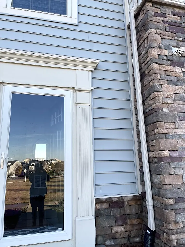 Clean blue lap siding and stone veneer beside a storm door after house washing