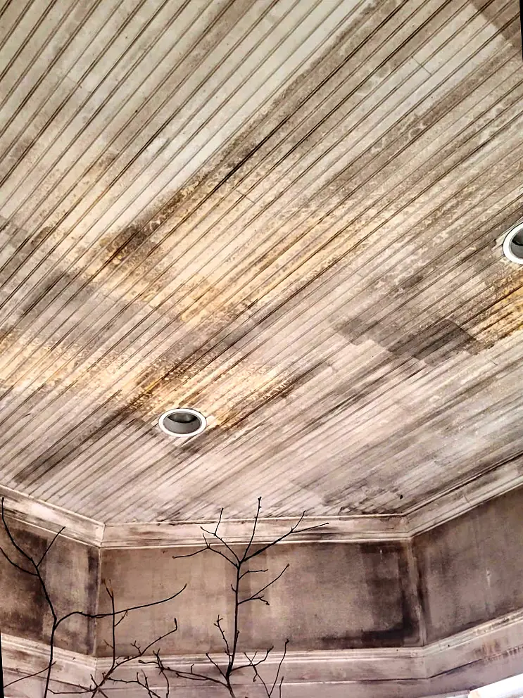 Before: Beadboard ceiling of an octagonal outdoor porch, stained dark with soot and smoke residue
