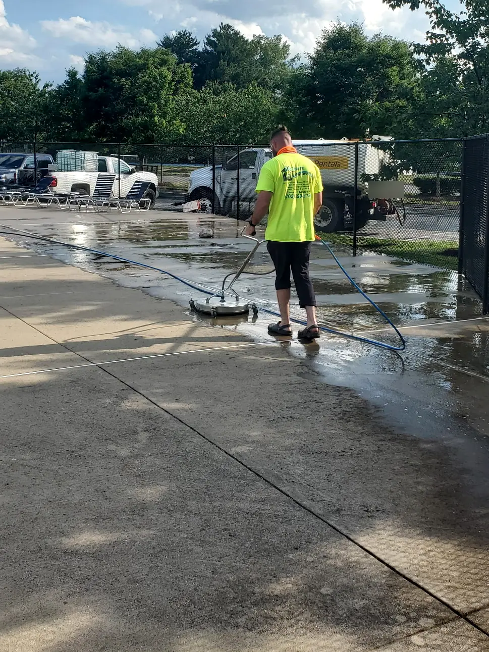 Crew member in a high-visibility Ultimate Powerwash shirt surface cleaning a community pool deck