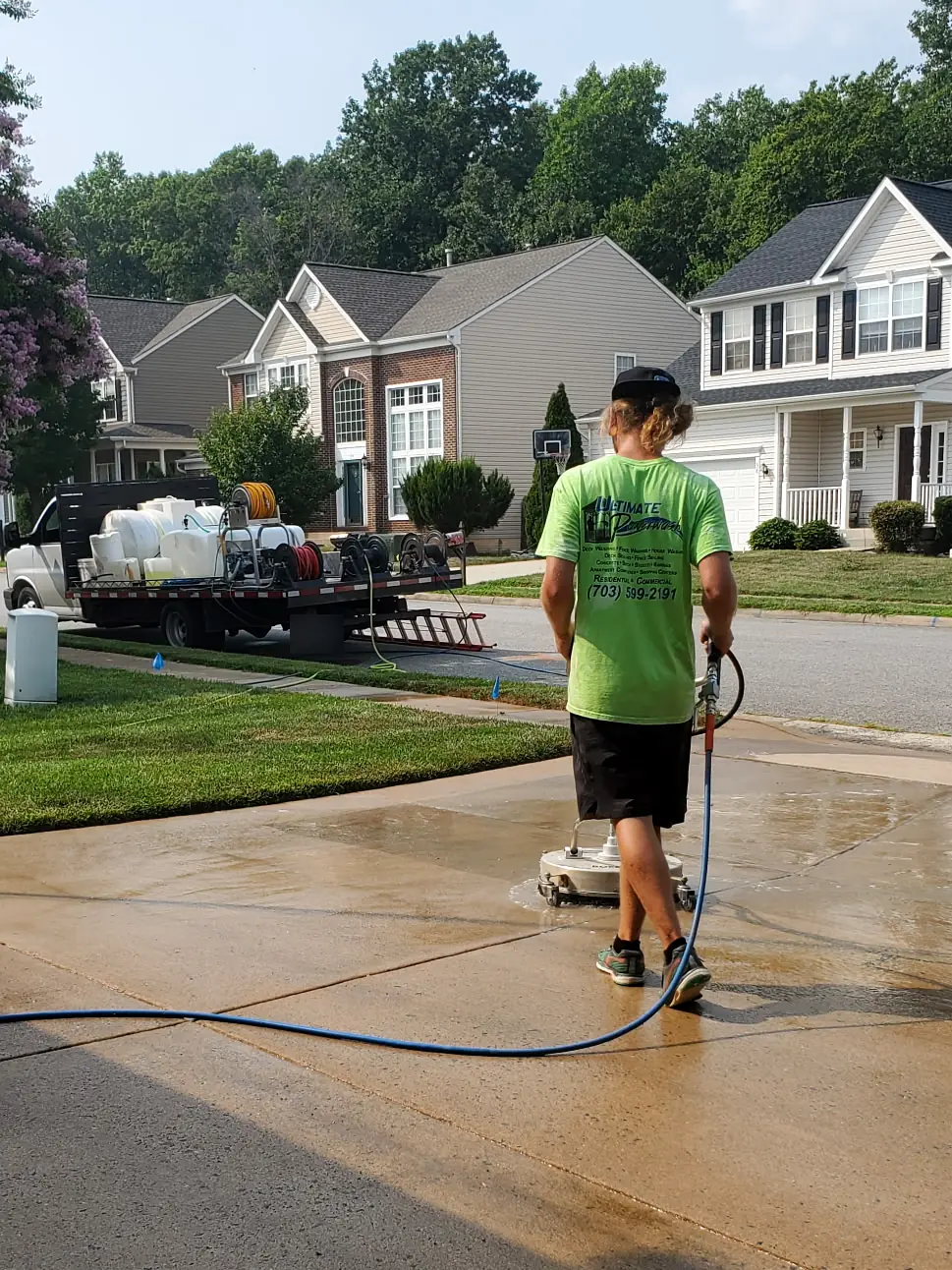 Ultimate Powerwash crew member running a surface cleaner on a concrete driveway, with the company rig parked at the curb