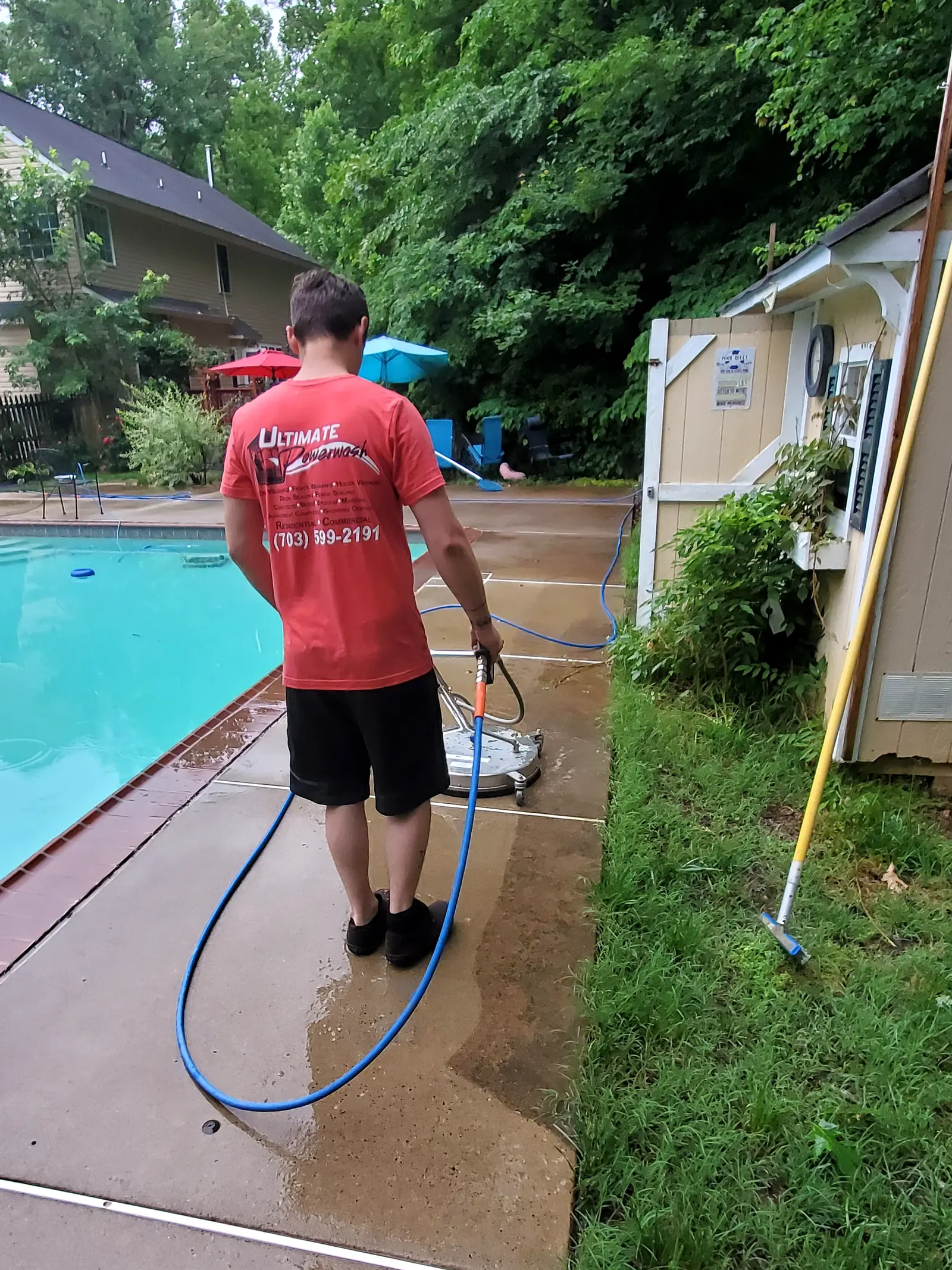 Ultimate Powerwash crew member running a surface cleaner along a backyard pool deck, leaving a clean path behind