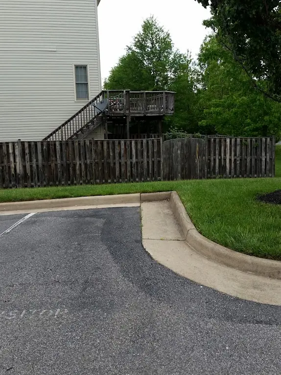 Before: Gray, weathered wood privacy fence and deck behind a townhouse, seen from the parking lot